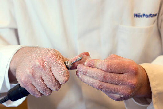 Ein Hörakustiker schleift ein Hörgerät zur individuellen Anpassung in der Werkstatt.